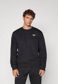 Czarna bluza z bawełnianej mieszanki, z okrągłym dekoltem, prążkowanymi mankietami i dołem, z małym białym logo Reebok na klatce piersiowej.