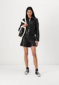 Svart lær cropped jakke med glidelås, sammen med svarte lær shorts og høytopp sneakers. Har en veske med hvit pelsdetalj.