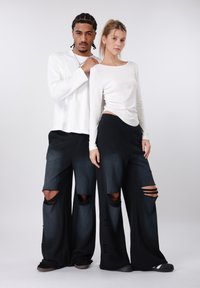 Μαύρο παντελόνι με φαρδιά πόδια και σκισίματα, συνδυασμένο με εφαρμοστά λευκά μπλουζάκια μακρυμάνικα. Φαίνεται λεία υφή, σαν βαμβακερή.