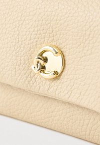 Κρεμ χρώματος υφής δερμάτινη επιφάνεια με γυαλιστερή χρυσή λεπτομέρεια κλειδώματος που συνδέεται σε διπλωμένη άκρη μιας τσάντας ή πορτοφολιού.