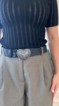 Črna rebrasta majica v kombinaciji s sivimi karirastimi hlačami visoko pasu. Debel črn usnjen pas z detaljno srebrno zaponko v obliki srca.