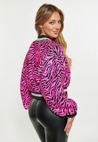 Roze, met pailletten bedekte bomberjack met zwarte zigzagpatronen en puffy mouwen. Beschikt over een zwarte ribcol van de kraag en manchetten, gestyled met slanke zwarte broek.