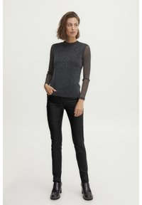 Haut noir à manches longues avec des manches transparentes texturées. La silhouette ajustée complète un pantalon noir ajusté et des bottes noires imposantes.