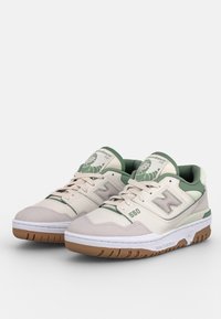 Chaussures de sport crème et vertes avec tige en suède et mesh, semelle en caoutchouc, et logo brodé. Présentent une conception à lacets et un col rembourré.