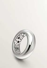 Anillo de plata con una superficie exterior lisa y redondeada y un interior hueco con recortes circulares, que muestra un diseño moderno.