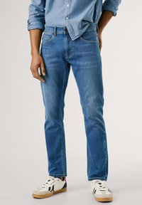 Jeans in denim blu chiaro con una vestibilità dritta e un leggero sbiadimento. Indossati con una camicia button-up blu chiaro e sneaker multicolori.