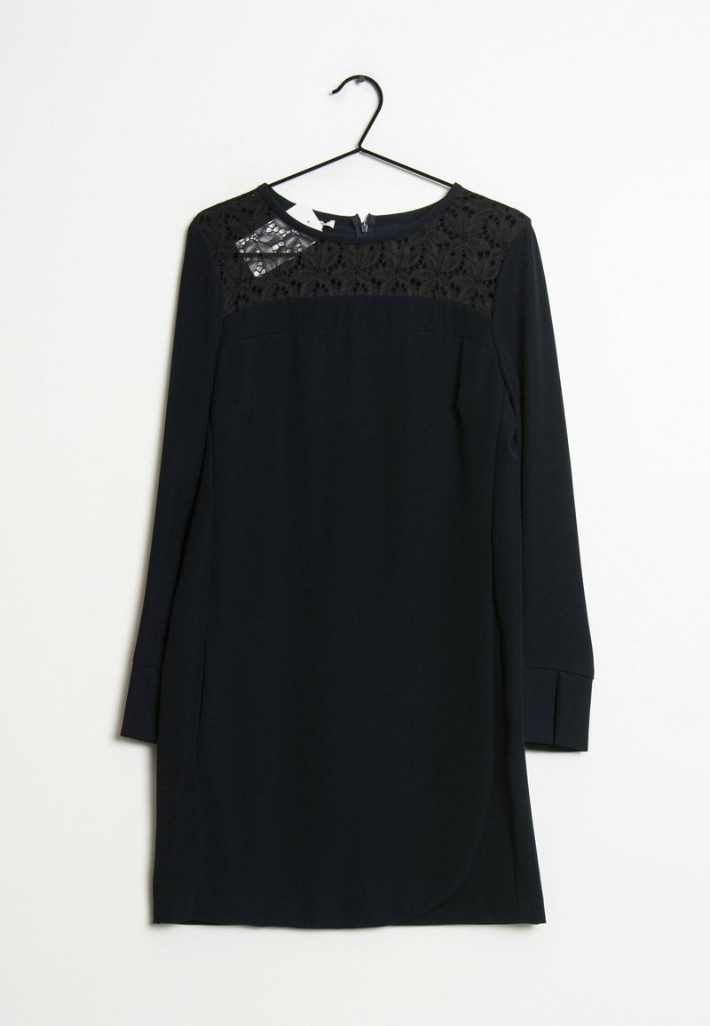 Robe noire avec des manches longues, des détails en dentelle sur le buste, un col rond et une jupe de texture lisse. Accrochée à un crochet noir.