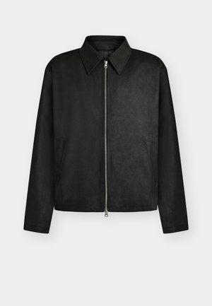 Veste noire zippée avec col pointu, manches longues et deux poches latérales, présentée sur un fond clair uni.