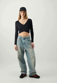Black ribbed crop top with long sleeves, loose light blue jeans, and black shoes with red accents. Model wearing a black cap.