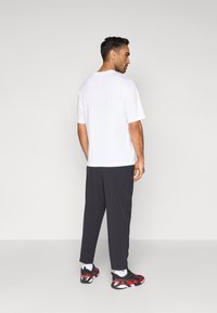 Λευκό κοντομάνικο πουκάμισο, μαύρο κωνικό παντελόνι και κόκκινα-μαύρα παπούτσια αθλητικά. Λείο ύφασμα με άνετη εφαρμογή και διακριτική ραφή.