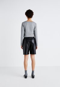 Harmaa pitkähiha-pusero, mustat nahkashortsit, harmaat sukat ja niititetyt mustat kengät. Sileät tekstuurit ja istuva leikkaus, näkyvät vetoketjut.