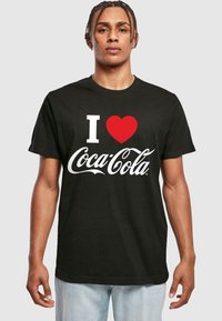Sort t-shirt med teksten "I ❤️ Coca-Cola" i hvid og rød, med en afslappet pasform og korte ærmer, lavet af bomuld eller lignende materiale.