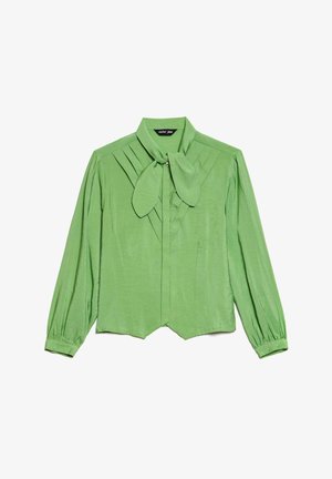 Blusa verde de manga longa com colarinho laço, apresentando pregas na parte da frente, uma forma estruturada e uma textura suave e brilhante.