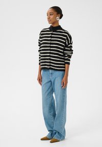 Zwart-wit gestreepte cardigan met hoge kraag, knopenvoorzijde en lange mouwen, gecombineerd met lichtblauwe wijde jeans en bruine puntige schoenen.