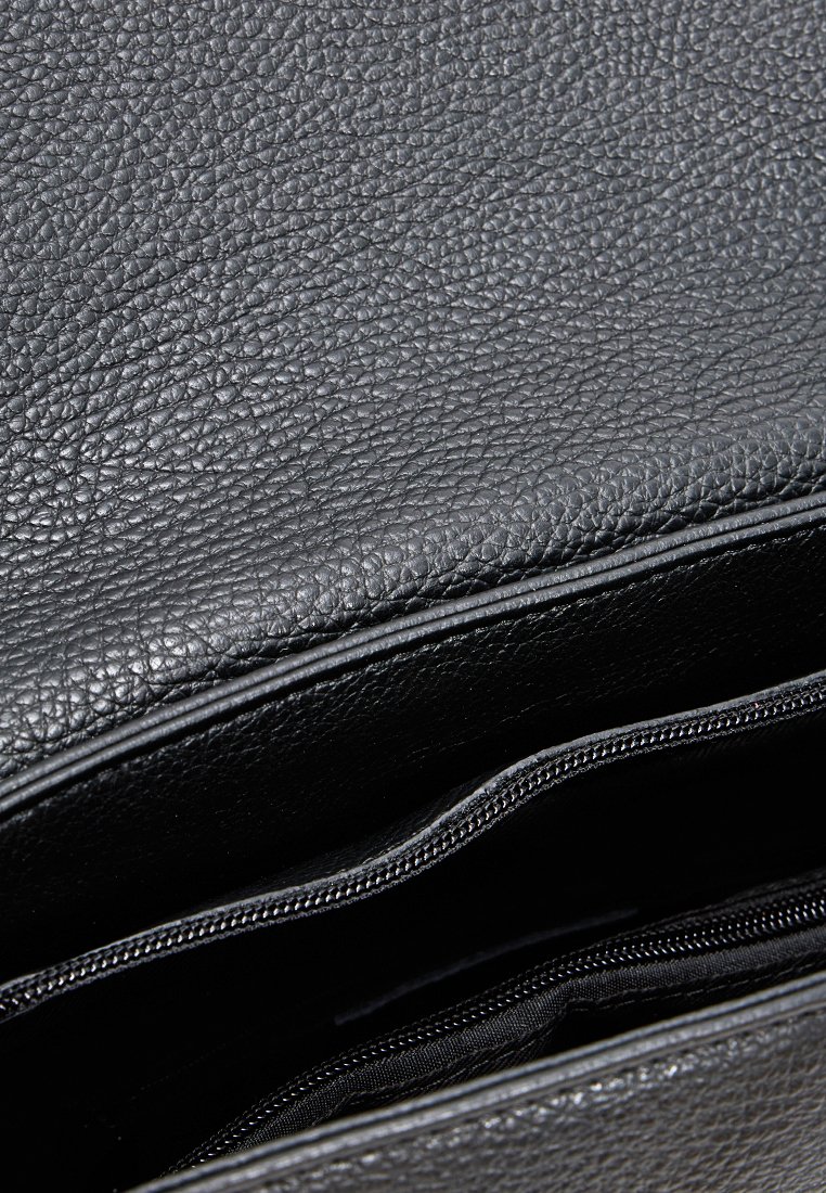 Sac en cuir noir texturé partiellement ouvert, montrant l'intérieur avec une poche zippée visible.