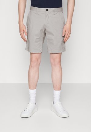 Beige bomulds shorts med flad front, sidelommer og knaplukning. Parret med hvide sneakers og ankellange hvide sokker.