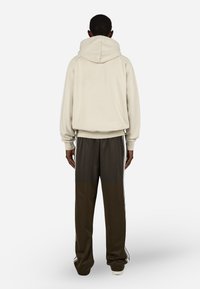 Φούτερ με κουκούλα σε κρεμ ύφασμα με άνετη εφαρμογή, συνδυασμένο με σκούρους ελαιοπράσινους τζόγκινγκ με λευκές πλαϊνές ρίγες και στενές γάμπες.