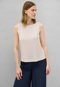 Top beige sin mangas, textura acanalada, cuello redondo, combinado con pantalones de pierna ancha en azul marino. Diseño simple, tejido ligero, sin acentos adicionales.