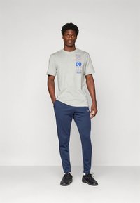 Szary t-shirt z krótkim rękawem z niebiesko-czerwonym nadrukiem, w połączeniu z granatowymi sportowymi spodniami z logo Nike oraz czarnymi butami sportowymi.