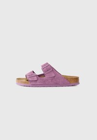 Pink suede sandals with two adjustable straps, cork footbed, and rubber sole featuring a textured finish and rounded shape.