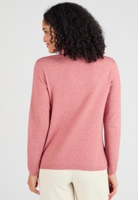 Maglione rosa con una trama morbida, maniche lunghe e colletto a costine. Presenta una vestibilità comoda, mostrato da dietro.