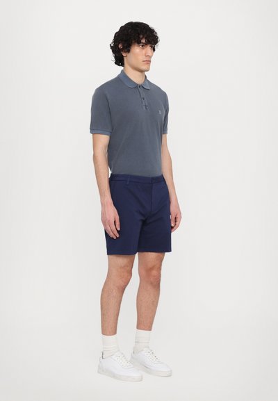 Polo gri cu mâneci scurte; pantaloni scurți bleumarin; adidași albi; material texturat ușor; prezintă un mic logo brodat pe piept.