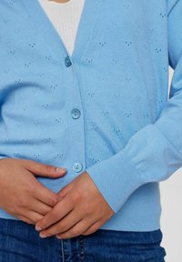 Světle modrý pletený cardigan s výstřihem do V, zapínáním na knoflíky, žebrovanými manžetami a malými otvory po celé látce.