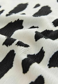 Tissu texturé noir et blanc présentant un motif de vache, avec des formes variées de taches noires sur un fond clair.