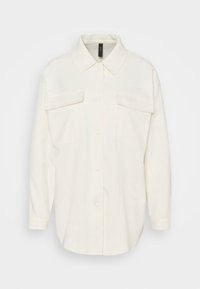 Kermanvärinen pitkähihaisen napillisen paidan, jossa on terävät kaulukset ja kaksi suurta läppätaskua rinnassa.