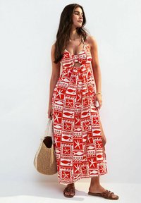 Rood en wit gemusterde maxi-jurk met spaghettibandjes, uitsnijding, zijsplitten en een vloeiende silhouette. Gecombineerd met een gevlochten tas.
