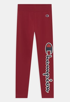 Leggings rouges avec le logo Champion sur la partie supérieure de la cuisse gauche et un grand texte vertical Champion avec emblème sur la jambe droite.