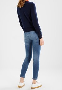 Navy knit sweater with long sleeves, fitted design, and button accents at cuffs, paired with blue skinny jeans and white sneakers.