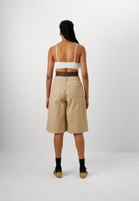 Beige, knielange Shorts mit lockerem Schnitt und sichtbaren Taschen, kombiniert mit einem himmelblauen Top mit dünnen Trägern und gemustertem Bund.