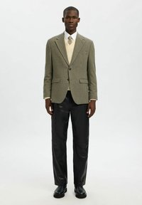 Ruuduline bleiser matt roheline, nööbitud, kreemja kampsuni peal, koos mustade nahkpükste ja kõrge säärega saapatega. Lihtne, kohandatud disain.