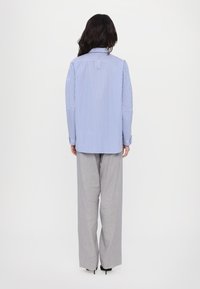 La camicia a righe blu e bianca ha maniche lunghe, un orlo arrotondato e una spalla sul retro. Abbinata a pantaloni grigi a vita alta.