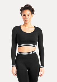 Sort langærmet cropped top med rund halsudskæring og hvide striber på ærmerne og linningen, lavet af et elastisk materiale.