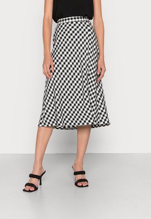 Jupe midi portefeuille vichy noir et blanc portée avec un top noir sans manches et des sandales noires à talons hauts avec brides froncées.