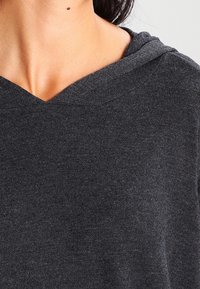 Mörkgrå hoodie gjord av mjukt tyg, med en V-ringning och en strukturerad yta, samt en huva och sömnadsdetaljer.