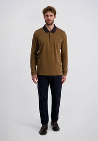Braunes Langarm-Polohemd mit einem marineblauen Kragen, strukturiertem Stoff, Knopfleiste und einem kleinen Logo auf der linken Brust, kombiniert mit marineblauen Hosen.