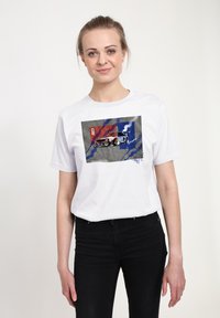 Hvid bomulds-t-shirt med et grafik af en racerbil på en tekstureret baggrund med røde og blå accenter. Korte ærmer og rund halsudskæring.