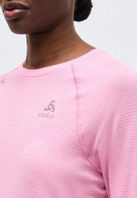 Κοντινό πλάνο ενός ατόμου που φοράει ροζ μακρυμάνικη μπλούζα με υφή, στρογγυλή λαιμόκοψη και μικρό λογότυπο "odlo" στο στήθος.