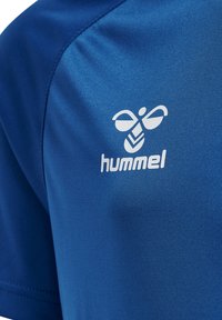 Camisa atlética azul hecha de una tela suave, con un logo "hummel" en blanco y un diseño estilizado de abeja en el hombro.
