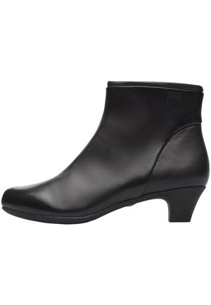 Must must täiendus musta naha põlvekõrguste saabastega, millel on sile tekstuur, ümar nina ja keskmise kõrgusega kontsad. Omab minimalistlikku disaini ja jõulist profiili.