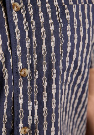 Navy blue shirt with cream vertical chain-link stripes, brown buttons, and a chest pocket on the left side.