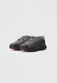 Tamsiai pilka Nike bėgimo batų pora su juodais banginiais padais ir oranžiniais swoosh logotipais ant balto fono.