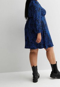 Blaues Tiermusterkleid mit langen Ärmeln, fließender Form und gerüschter Taille. Getragen mit schwarzen Ankle Boots mit einer robusten Sohle.