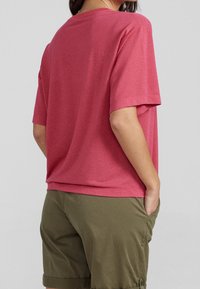 Tričko s krátkým rukávem a kulatým výstřihem vyrobené z melírované růžové tkaniny, v kombinaci s olivově zelenými šortkami, které mají uvolněný střih a jemnou texturu.