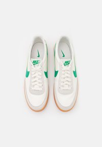 Weiße Ledersneaker mit grünen Akzenten. Sie verfügen über eine Sohle aus Gummirubber, eine runde Zehenpartie und ein Schnürdesign. Nike-Branding auf der Zunge und an den Seiten.