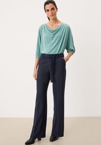 Lichtblauw drapeertop met 3/4 mouwen, gecombineerd met hooggewaiste marineblauwe broek met een strikceintuur en een gladde textuur. Zwarte hakken laarzen.