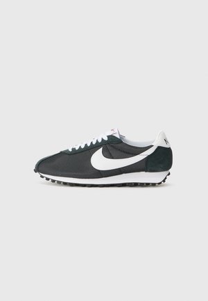 Sort og hvid Nike løbesko med mesh-overdel, hvide snørebånd og vaffelsål, vist i sideprofil på grå baggrund.